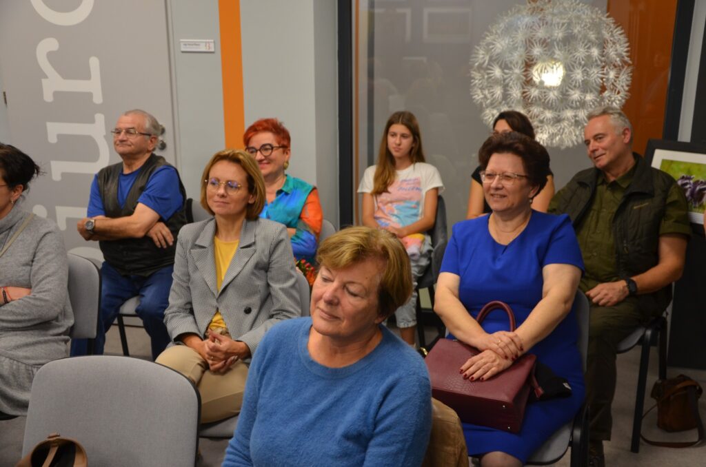 Na zdjęciu przedstawieni są uczestnicy otwarcia wystawy fotografii. Na zdjęcij widoczni są kobiety, mężczyzna po lewej stronie.