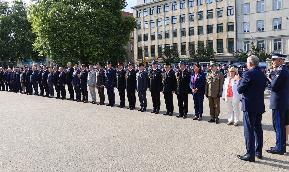 Wręczenie medali za Zasługi dla Policji. W rzędzie stoją władze samorządowe. W tle znajduje się budynek.