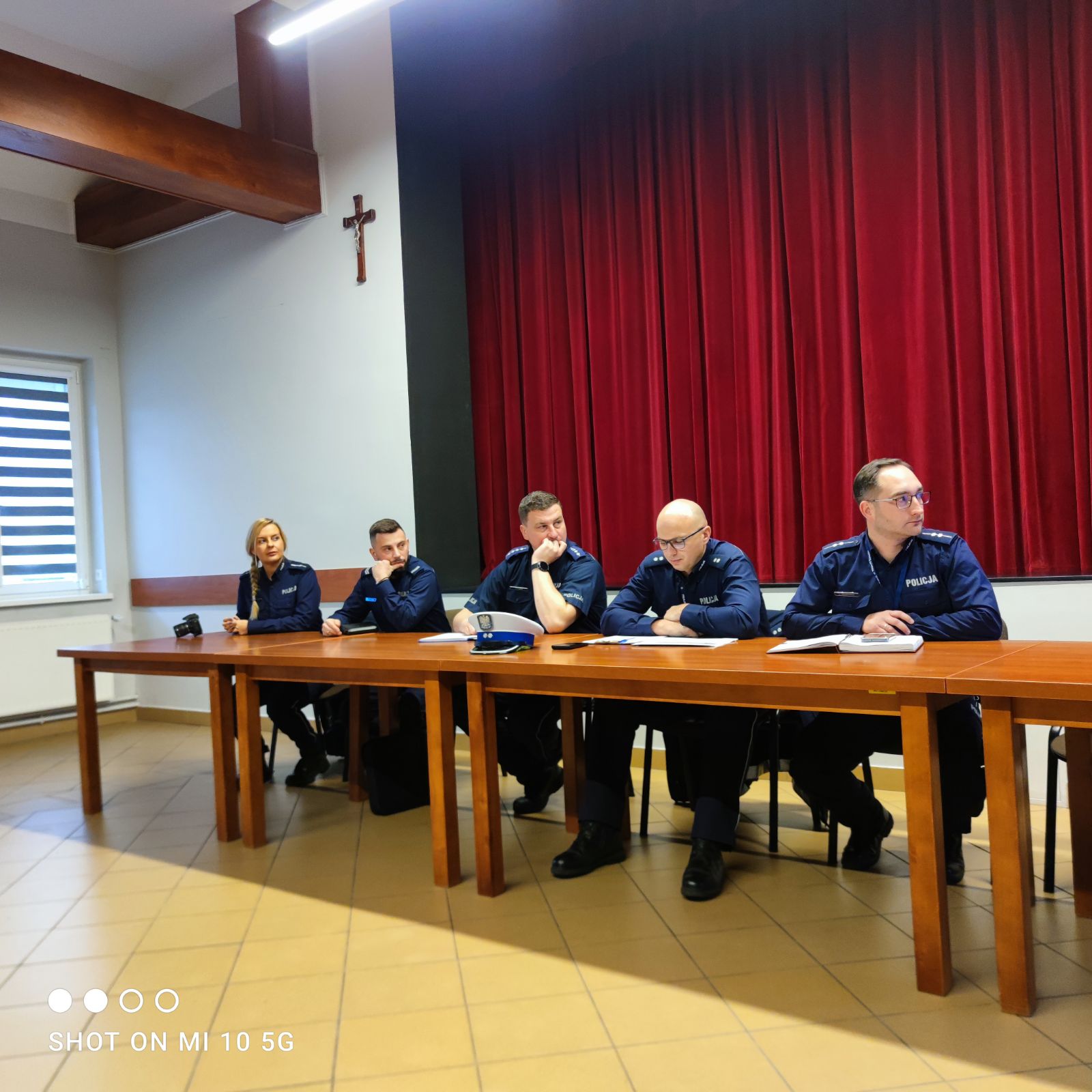 Przy stole siedzą 5 funkcjonariuszy z&nbsp;komendy policji w&nbsp;nowym tomyślu oraz&nbsp;z terenu gminy miedzichowo. Stoły są w&nbsp;kolorze ciemno brązowym oraz&nbsp;krzesła też są w&nbsp;kolorze ciemnym. Za Funkcjonariuszami znajduje się scena. 