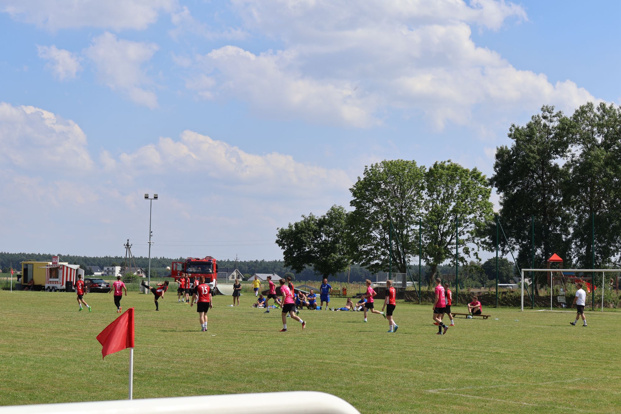 Stadion sportowy, na boisku grają drużyny zgłoszone do turnieju, w swoich strojach piłkarskich.