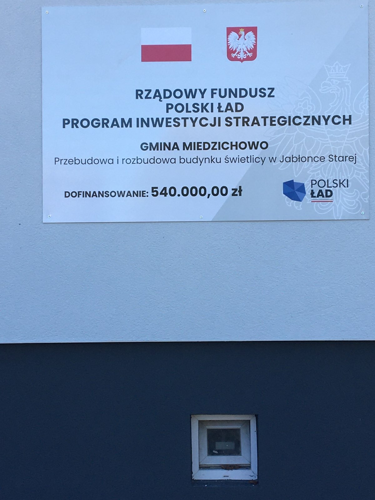 Na zdjęciu przedstawiona jest tablica, która informuje"Rządowy Fundusz Polski Ład Program Inwestycji Strategicznych Gmina Miedzichowo Przebudowa i rozbudowa budynku świetlicy w Jabłonce Starej Dofinansowanie 540.000,00 zł.