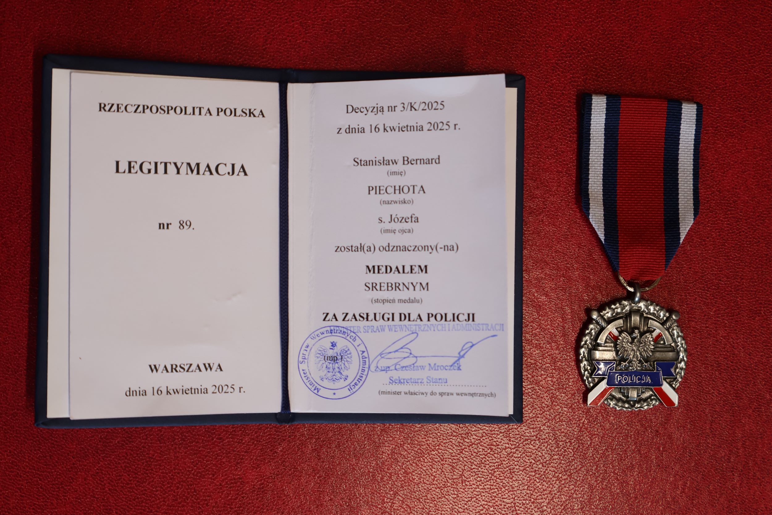 Na pierwszym planie znajduje się książeczka z&nbsp;odznaką, na&nbsp;czerwonym tle. 