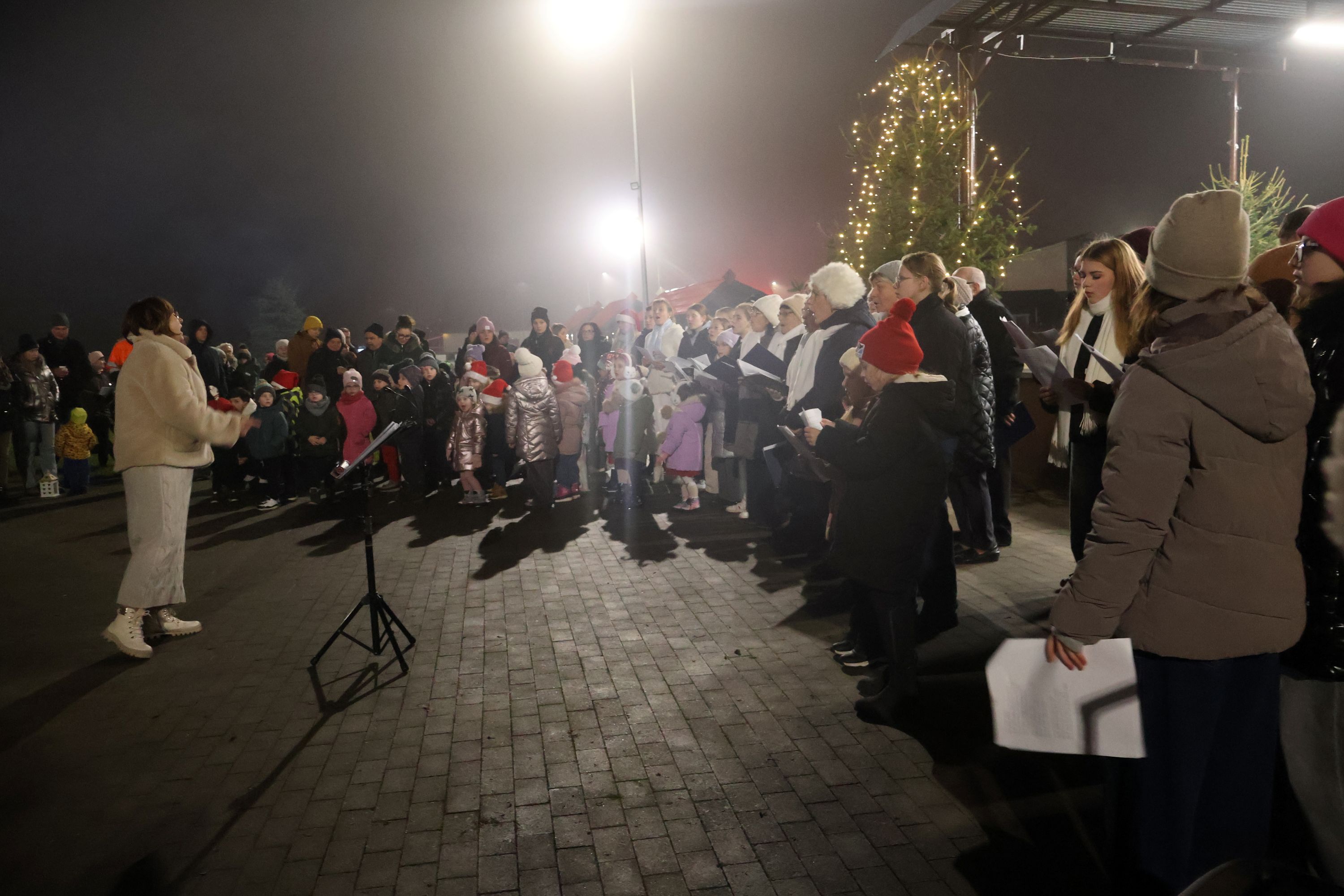 Grupa ludzi śpiewająca przed sceną. 