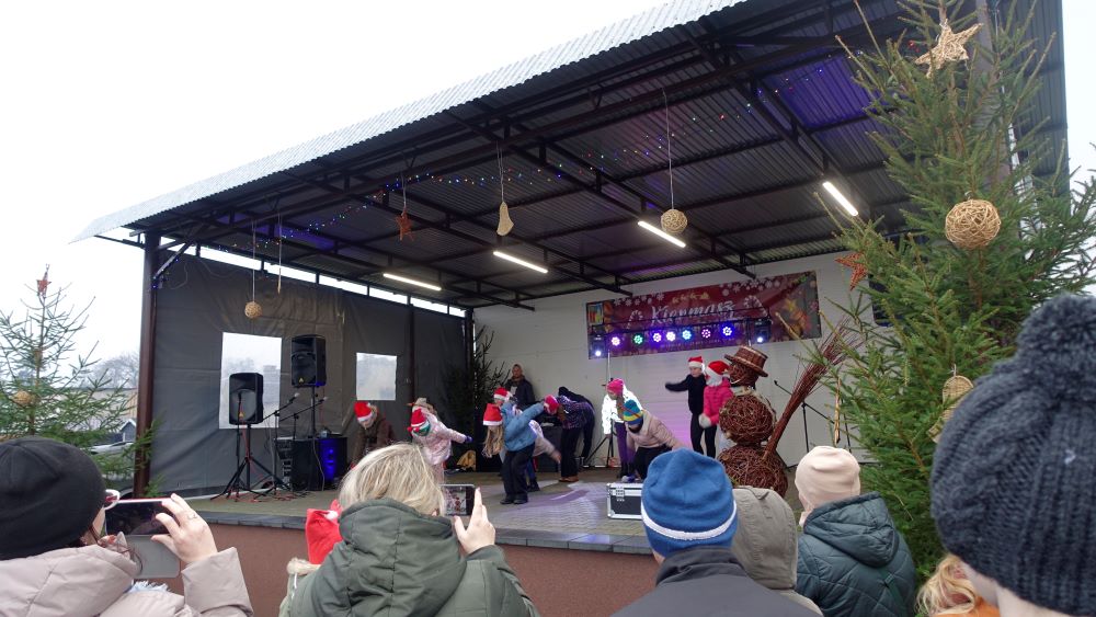 Na scenie wystepują dzieci. Ubrane są na&nbsp;kolorowo. Przed sceną stoją rodzice oraz&nbsp;uczestnicy Kiermaszu Bożonarodzeniowego.