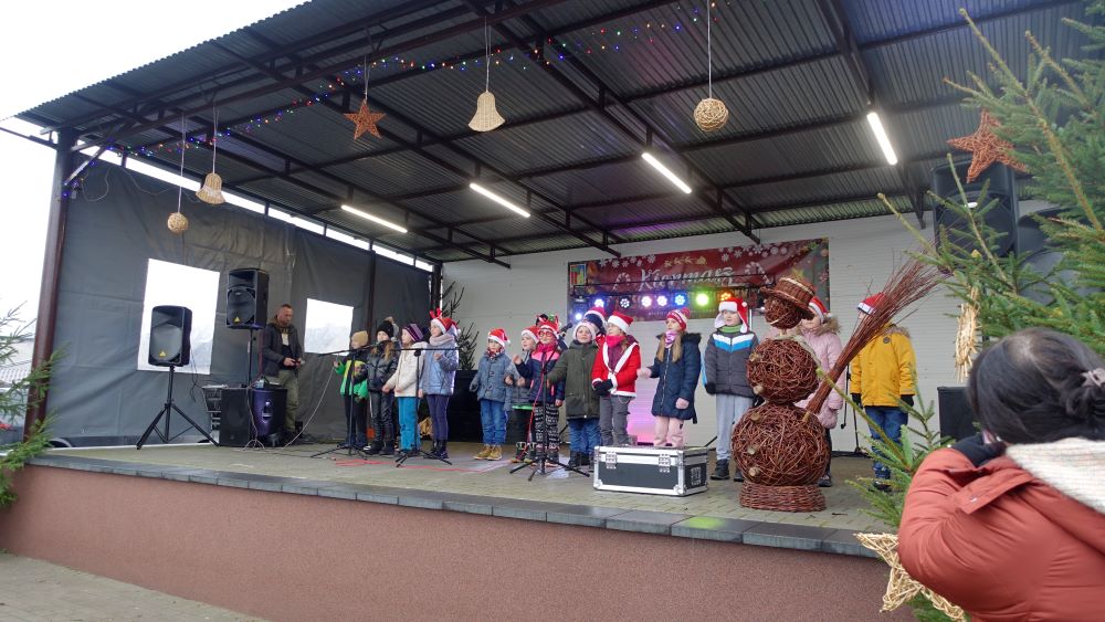 Na scenie wystepują dzieci. Ubrane są na&nbsp;kolorowo. Przed sceną stoją rodzice oraz&nbsp;uczestnicy Kiermaszu Bożonarodzeniowego.