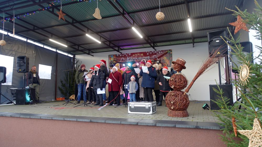 Występ podopiecznych z&nbsp;Warsztat&oacute;w Terapii Zajęciowej w&nbsp;Grońsku. Podopieczni występują na&nbsp;scenie, kt&oacute;ra jest wystrojona w&nbsp;dekoracje świąteczne.