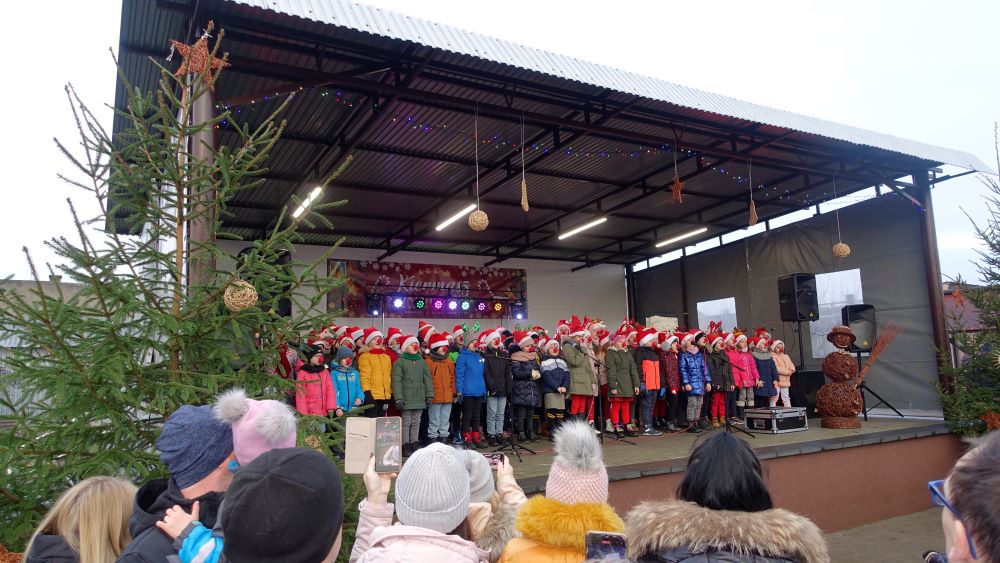Na scenie wystepują dzieci. Ubrane są na&nbsp;kolorowo. Przed sceną stoją rodzice oraz&nbsp;uczestnicy Kiermaszu Bożonarodzeniowego.