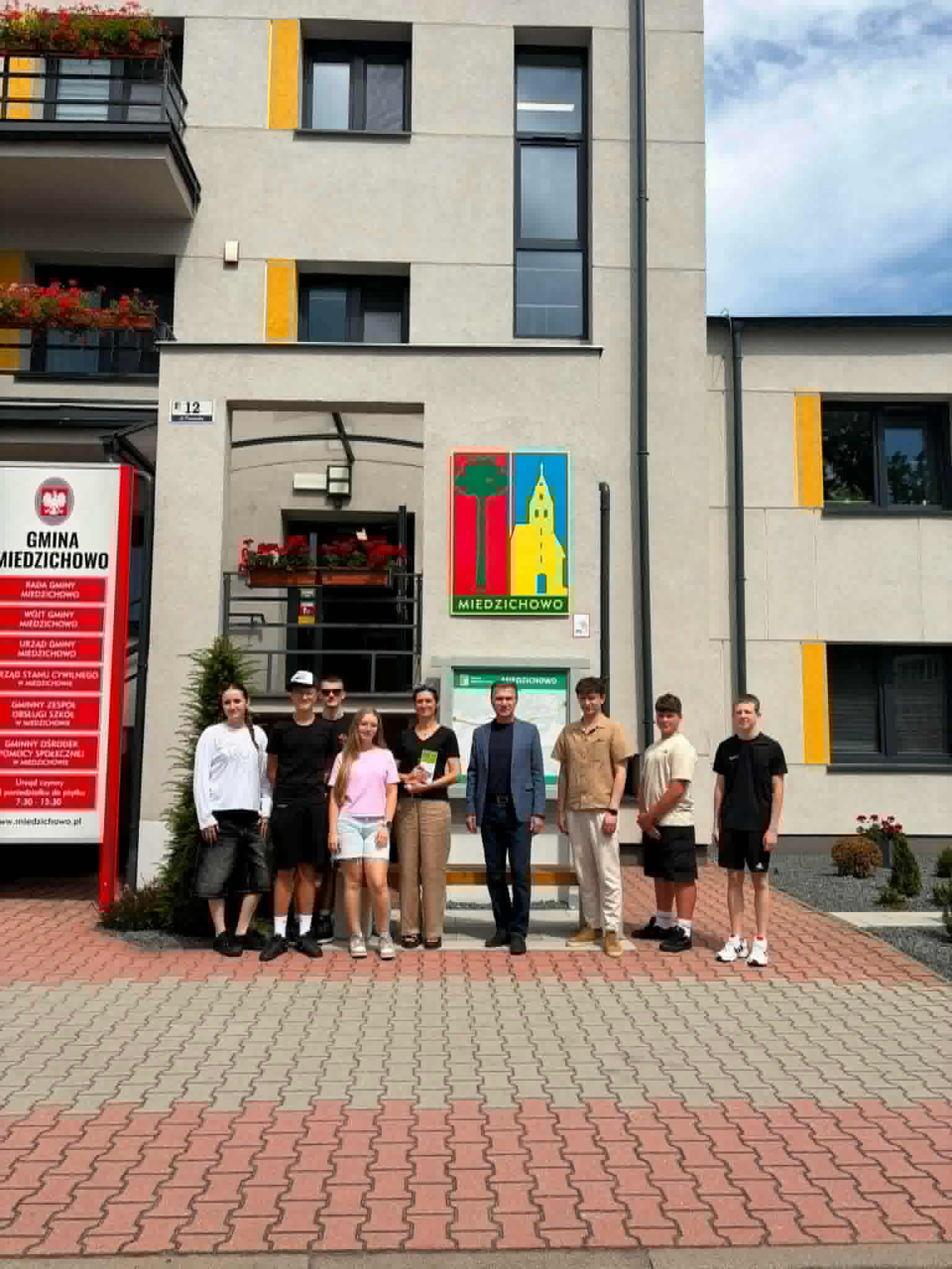 Młodzież stojąca na&nbsp;tle budynku Urzędu Gminy wraz z&nbsp;opiekunami.